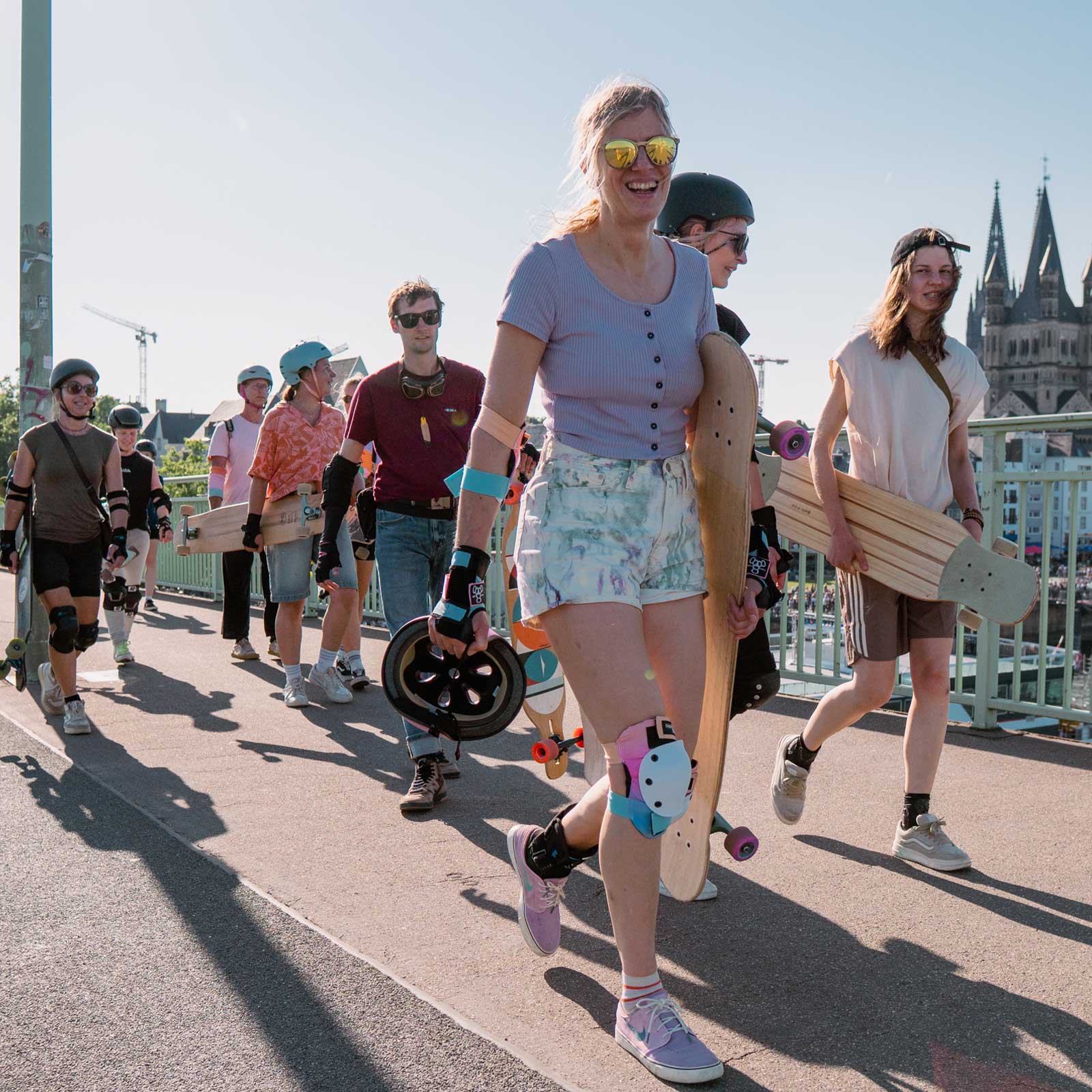 Die Teilnehmenden vom Longboard Camp Grow Your Flow laufen über die Brücke in Köln