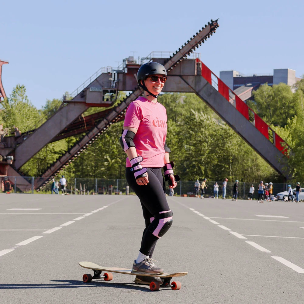 Eine Frau in einem pinken Tshirt steht an der Zeche Zollverein in Essen auf einem Longboard