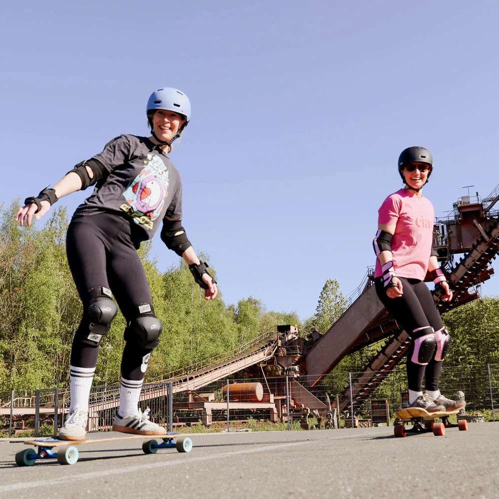 Eine Frau in einem pinken Tshirt steht an der Zeche Zollverein in Essen auf einem Longboard